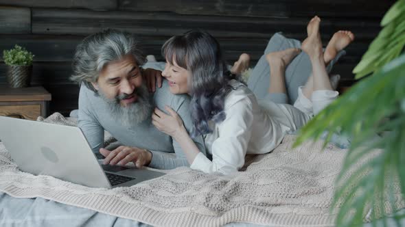 Slow Motion of Man and Woman Using Laptop Lying in Bed Talking and Laughing alt