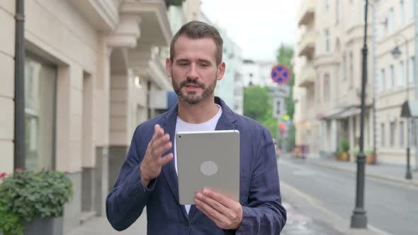 Mature Adult Man Talking on Video Call on Tablet While Walking Down the Street alt