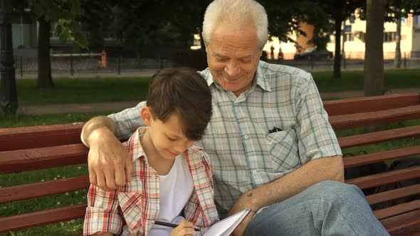 Little Boy Writes in His Notebook What His Grandpa Says
