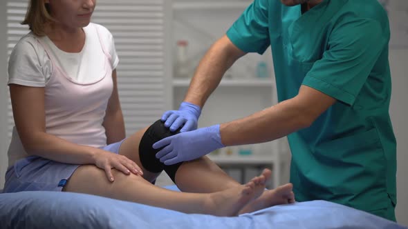 Surgeon Checking Position of Knee Brace on Female Patient Leg, Rehabilitation