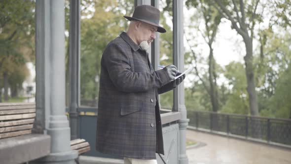 Side View of Elegant Confident Man in Hat and Leather Gloves Writing in Notebook, Hiding Notes, and alt