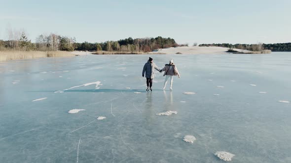 Aerial Shot of Couple Skating on a Blue Frozen Lake in Beautiful Sunny Landscape alt