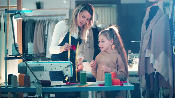 A Seamstress is Teaching a Girl to Work with Fabric alt