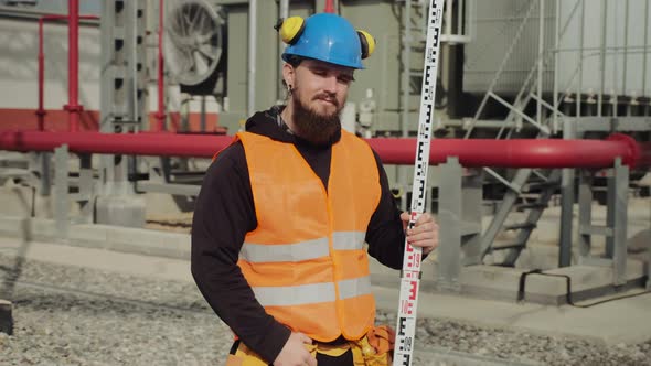 Bearded Engineer Holds Geodetic Pole Posing at Power Station