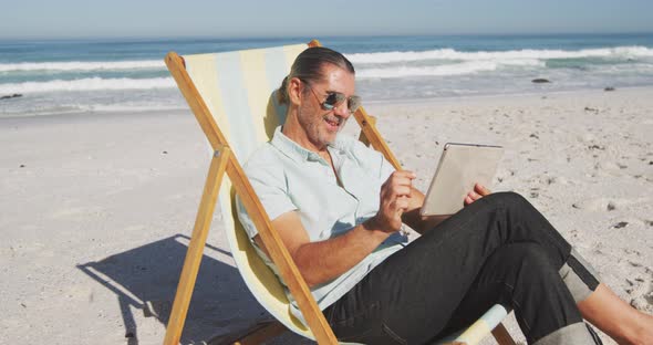 Senior Caucasian man sitting on sunbeds at the beach. alt