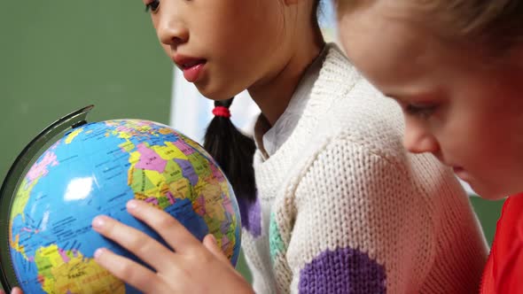 School kids looking at globe in classroom at school alt