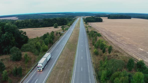 Cars Drive on One Lane of Long Road Stretching Between Trees alt