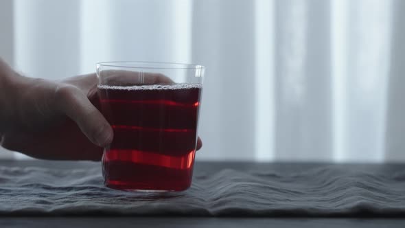 Slow Motion Man Hand Take Red Drink in Tumbler Glass From Black Wood Table with Copy Space alt