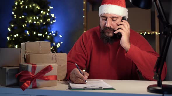 Dropshipping Owner Male Indian Santa Claus Works at Home Office at Night Taking Order By Phone and alt