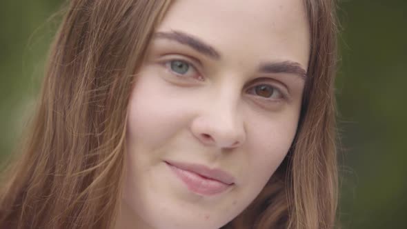 Close-up Portrait of Cute Carefree Young Woman with Different Colored Eyes Looking at Camera Indoors alt