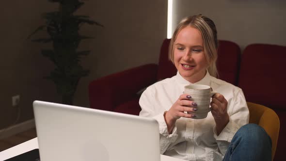 Smiling Surprised Young Woman Sitting at Home with a Cup of Coffee Using Laptop Has Video Chatting alt