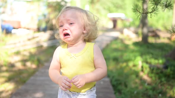 Close Up Portrait of Little Funny Cute Blonde Girl Child Toddler in Yellow Bodysuit Crying Outside