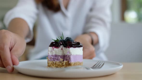 Closeup of a woman eating a piece of blueberry cheesecake