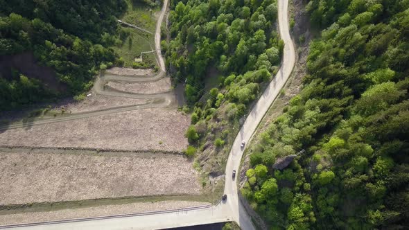 Aerial Top down shot of cars driving on road along reservoir with trees in the foreground alt