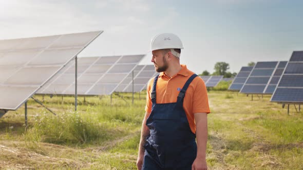 Industrial Man Engineer in Uniform Walking Through Solar Panel Field for alt