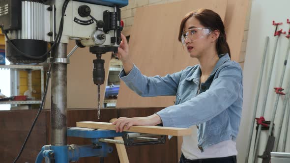female carpenter using drill machine on wood in a workshop