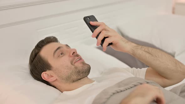 Video Chat on Smartphone By Young Man Laying in Bed alt