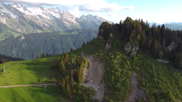 Drone Shot of Rugged Pine-Covered Mountain revealing a Snowy and Rocky Mountain Range in the Backgro alt