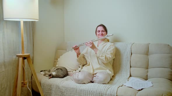 Happy woman with a flute is playing at home on the sofa in the living room alt