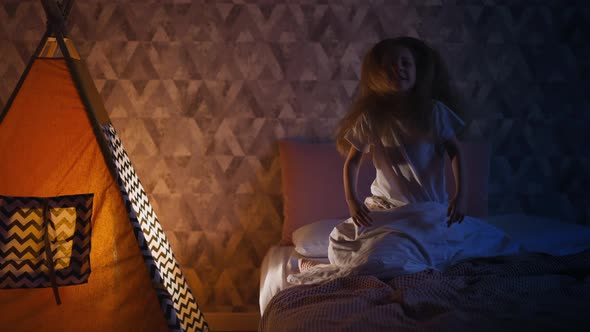 Active Little Child Has Fun on Bed at Play Teepee in Evening alt