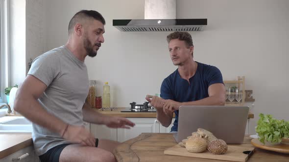 Gay male couple disagreeing and arguing in kitchen at home in the morning