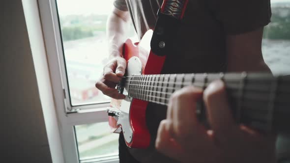 Close Up of Young Man Playing on Red Electric Guitar Funk or Blues Next To Window. Slow Motion