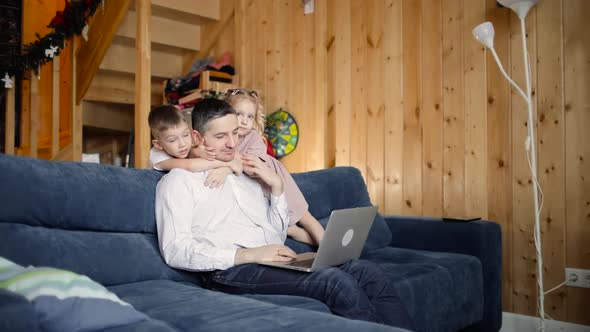 Father Is Trying To Work on Laptop with His Children Cuddling Him at Home