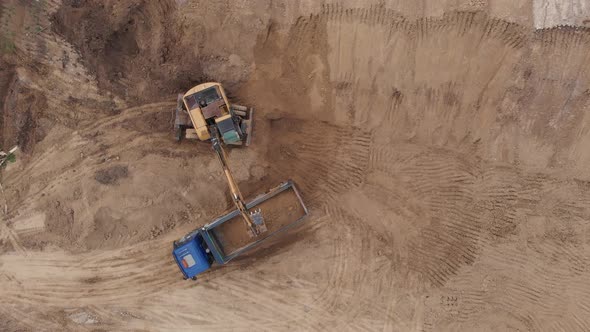Aerial top view: yellow excavator pouring soil into tipper. alt