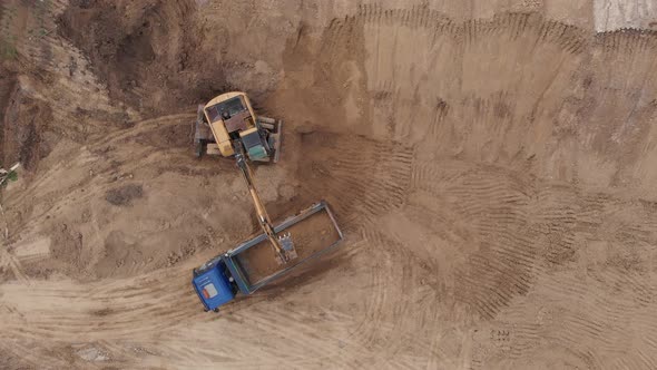 Aerial top view: yellow excavator pouring soil into tipper.