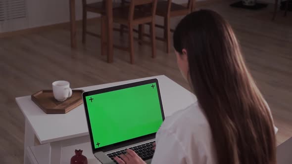 Home Isolated. Woman at Home Sitting on a Couch Works on a Laptop Computer with Green Mock-up Screen