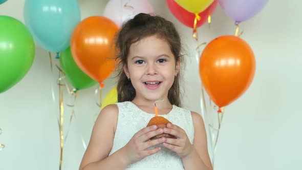 Girl in Dress Smiles Holding Cupcake with Burning Candle alt