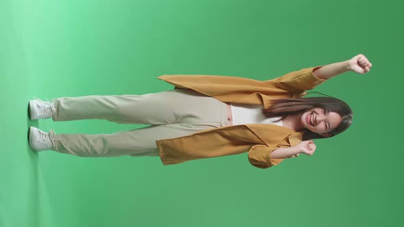 Full Body Of Cheerful Young Asian Woman Celebrating While Standing On Green Screen In The Studio alt