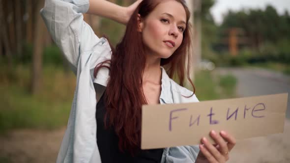 Gorgeous Redhead Young Woman with Future Banner Standing at Forest on Suburban Road Waiting for Car alt