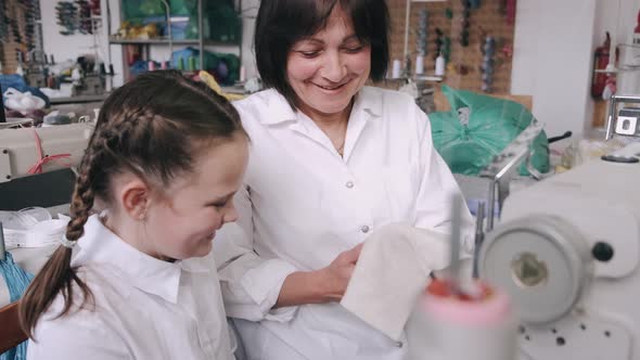Grandma with Little Granddaughter Sew Clothes in the Factory alt