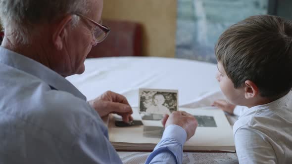 Friendly Grandfather with His Beloved Grandson Shows Photos of Youth Rejoicing in Memories of Youth alt