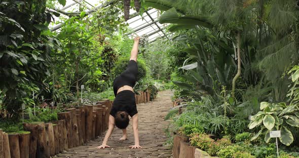 A Pretty Brunette Woman is Doing Yoga Exercises in a Beautiful Botanical Garden Standing with Bare