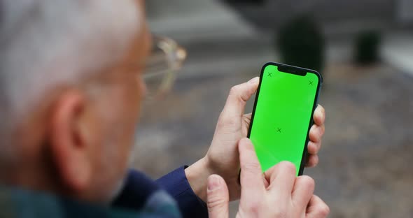 A Warmly Dressed Man Holds a Green Screen Phone alt