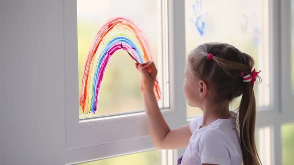 Kid painting rainbow during Covid-19 quarantine at home.