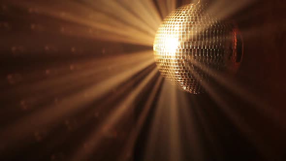 Shiny disco ball with golden reflection and rays in haze