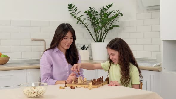 Cheerful Daughter Wins Mom in Chess and Rejoices While Sitting at the Table at Home alt