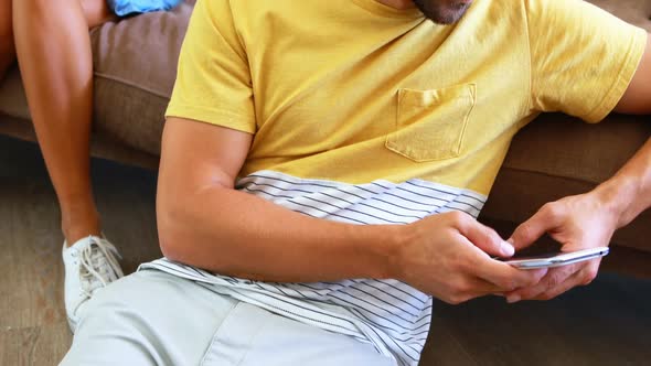Man text messaging and woman peeking into his mobile phone from behind alt
