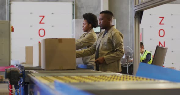 African american male and female workers with boxes on conveyor belt in warehouse alt
