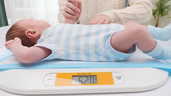 Young Caring Mother Stroking Her Little Newborn Baby Son While Weighing Him on Digital Scales in alt
