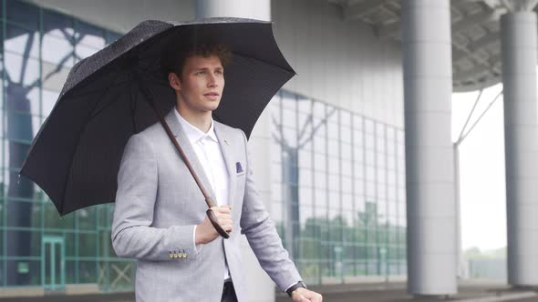 Handsome Businessman Standing Under Rain Near Airport Holding Umbrella Looking Around Waiting for