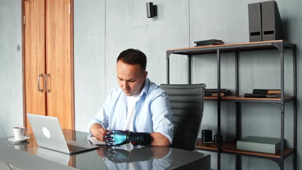 Concentrated cyborg man hacker with artificial limb looks at laptop display alt