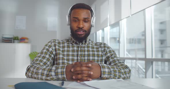 Cheerful Black Man in Headphones Has Video Call on Laptop From Office alt