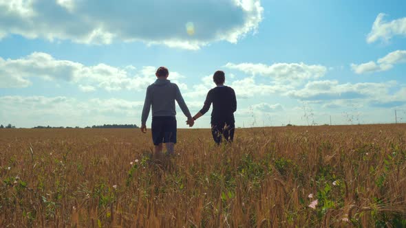 A Young Man and a Girl Are Holding Hands Walking Along a Cereal Field alt
