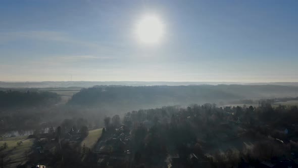 Aerial View of Forest and Farmland During Foggy and Cold Winter Morning with Blue Sky Facing the Sun alt