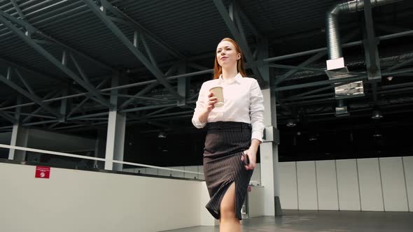female leader walks through lobby of business center with a phone and cup coffee alt