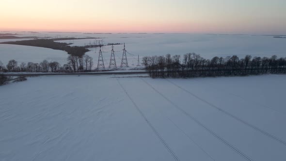 Aerial Drone View on Power Lines Over the Snowy Field at Sunset